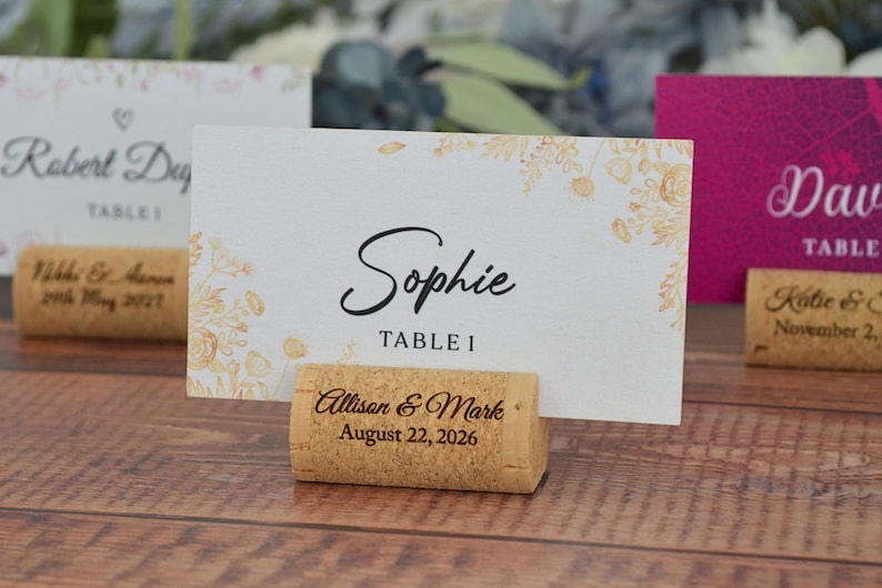 Personalized cork card holder, used for place cards for rustic style weddings, wedding favors, anniversaries, parties and birthdays. On a wooden base with decorative flowers. A beautiful decoration for weddings.