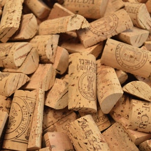 Puede incluir: Un primer plano de un montón de tapones de vino usados. Los tapones son de corcho natural y tienen una variedad de formas y tamaños. Algunos de los tapones tienen escritura en ellos, incluyendo las palabras "Tbilvino" y "A.R.F.C.B."