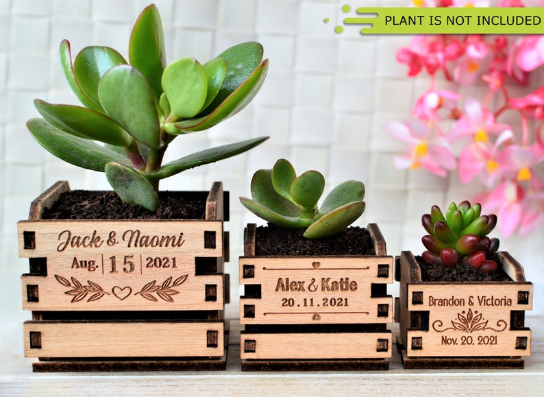 Engraved personalized mini pots, used for wedding favors, rustic style wedding decorations and your home. It is made of wood, with a succulent plant on a wooden table decorated with flowers. An excellent gift for guests and all your loved ones.