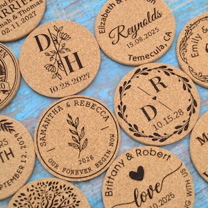 May include: A collection of ten round cork coasters with various personalised designs and text. The coasters feature a variety of designs, including a bridge, a heart, a tree, and initials. The text on the coasters includes names, dates, and locations.