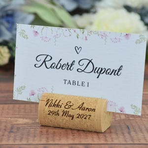 Personalized cork card holder, used for place cards for rustic style weddings, wedding favors, anniversaries, parties and birthdays. On a wooden base with decorative flowers. A beautiful decoration for weddings.