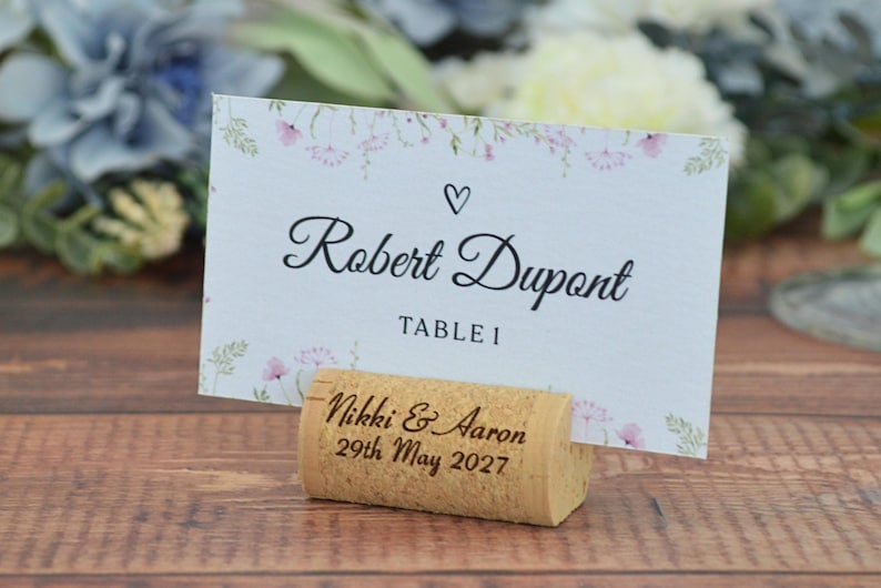 Personalized cork card holder, used for place cards for rustic style weddings, wedding favors, anniversaries, parties and birthdays. On a wooden base with decorative flowers. A beautiful decoration for weddings.
