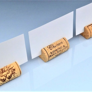 Cork card holders, perfect for wine themed weddings, rustic weddings, parties and anniversaries, these are from different vineyards and labels. 100% Natural High Quality cork with perfect cuts. On a white table with decorative flowers.