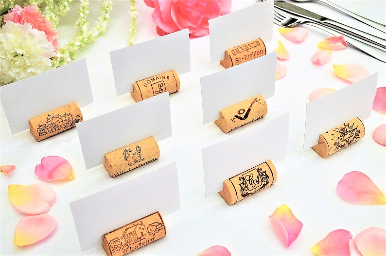 Cork card holders, perfect for wine themed weddings, rustic weddings, parties and anniversaries, these are from different vineyards and labels. 100% Natural High Quality cork with perfect cuts. On a white table with decorative flowers.