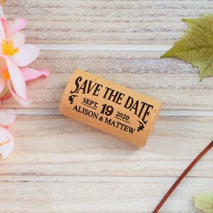 Personalized Save the Date corks for wine with wooden box and with or without magnets, used in wine themed weddings, and rustic weddings. It is made of 100% Natural High Quality Cork. On a glass plate with decorative flowers.