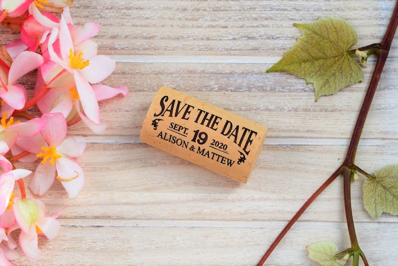 Personalized Save the Date corks for wine with wooden box and with or without magnets, used in wine themed weddings, and rustic weddings. It is made of 100% Natural High Quality Cork. On a glass plate with decorative flowers.