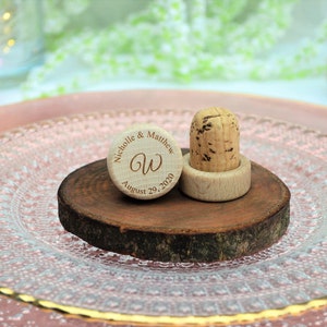 Personalized wine stopper, laser engraved, design 24, perfect for decorating rustic style weddings, parties and anniversaries. 
Made of wood and cork, on a table with decorative flowers. An excellent wedding favor for guests