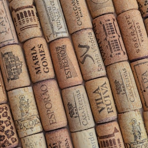 Puede incluir: Primer plano de una colección de corchos de vino usados, cada uno con textos y diseños impresos únicos. Los corchos son de varios tonos de marrón y beige, con texto en negro y otros colores. La disposición sugiere un tema relacionado con el vino.
