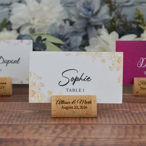 Personalized cork card holder, used for place cards for rustic style weddings, wedding favors, anniversaries, parties and birthdays. On a wooden base with decorative flowers. A beautiful decoration for weddings.