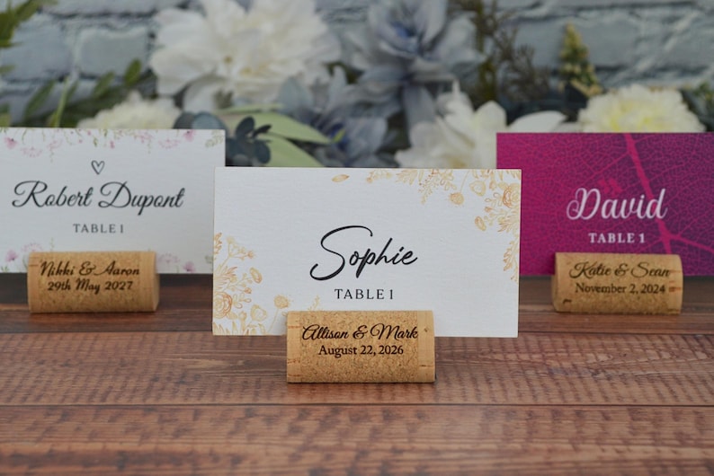 Personalized cork card holder, used for place cards for rustic style weddings, wedding favors, anniversaries, parties and birthdays. On a wooden base with decorative flowers. A beautiful decoration for weddings.