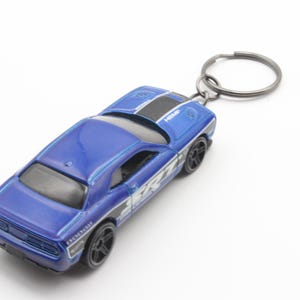 May include: A blue Dodge Challenger keychain with a black stripe and silver accents. The keychain is attached to a silver metal ring.