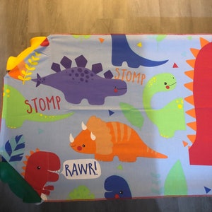 May include: A blue fabric play mat with a dinosaur theme. The mat features a purple dinosaur with the word "STOMP" written next to it, a green dinosaur, an orange dinosaur with the word "RAWR!" written next to it, and a red dinosaur.