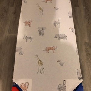 May include: A white fitted sheet with a repeating pattern of safari animals, including giraffes, zebras, elephants, tigers, and hippos. The sheet is bordered with red, blue, and yellow fabric.