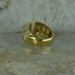 May include: A gold ring with a white mother-of-pearl inlay. The ring is set with a geometric pattern of squares.