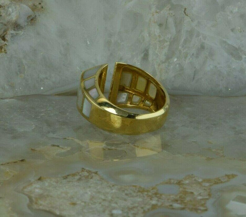 May include: A gold ring with a white mother-of-pearl inlay. The ring is set with a geometric pattern of squares.
