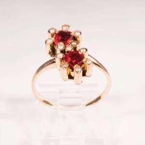 May include: A gold ring with two red gemstones surrounded by white pearls.