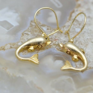 May include: A pair of gold dolphin earrings with a dangling design. The dolphins are facing forward with their tails curled up.
