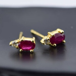 May include: A pair of gold earrings with a ruby and diamond accents. The earrings are oval shaped and have a polished finish.