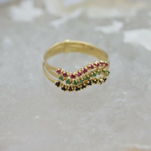 May include: A gold ring with three bands of gemstones. The top band has red gemstones, the middle band has green gemstones, and the bottom band has black gemstones.