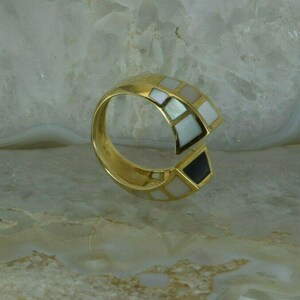 May include: A gold ring with a white and black geometric design. The ring is made of metal and has a smooth finish.