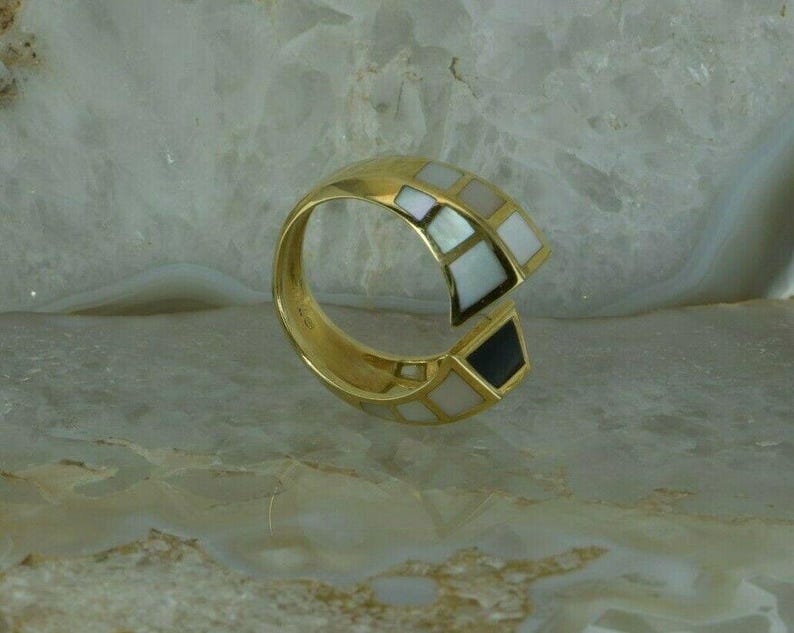 May include: A gold ring with a white and black geometric design. The ring is made of metal and has a smooth finish.