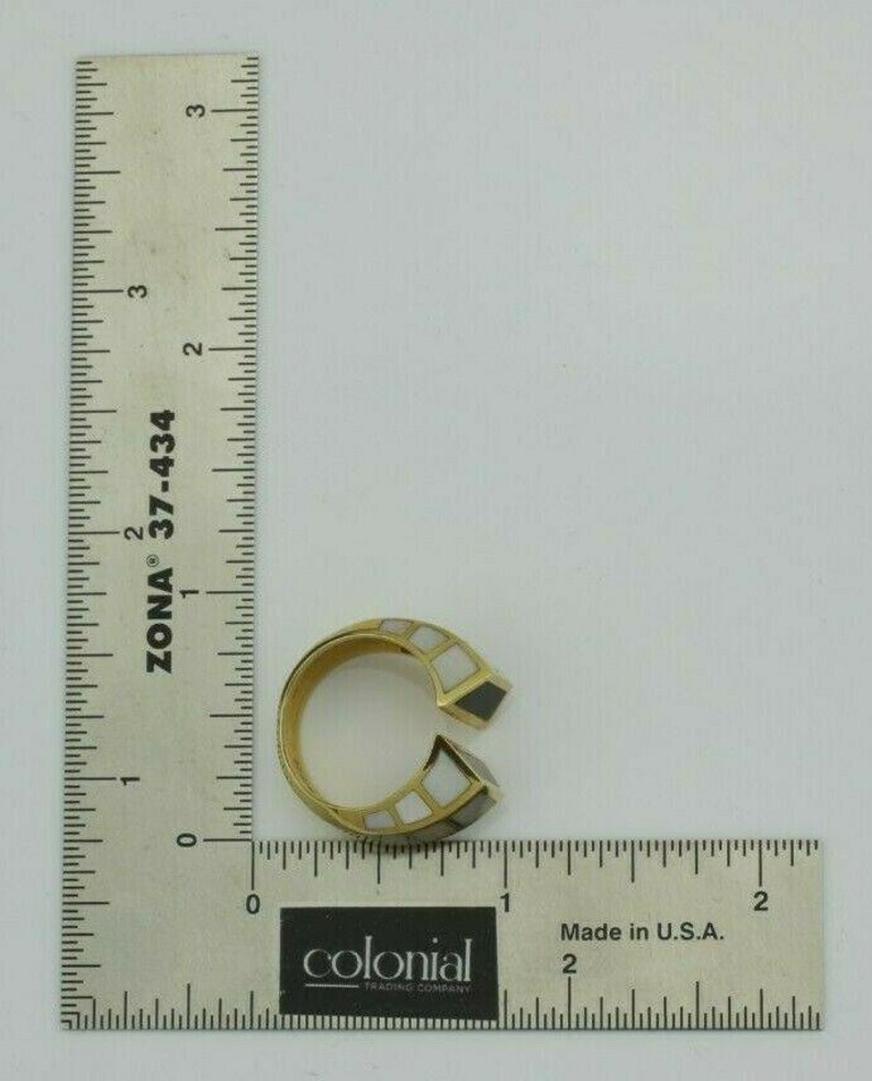 May include: A gold ring with black and white inlay. The ring is open on one side and has a geometric design.