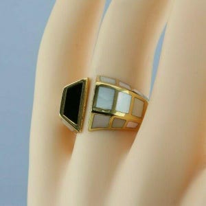 May include: A gold ring with a black and white geometric design. The ring is made of gold and has a black stone on one side and a white stone on the other.