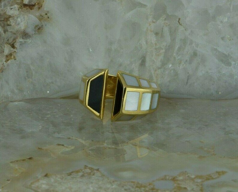 May include: A gold ring with a geometric design. The ring is made of two pieces, one black and one white, that fit together. The white piece is made of mother-of-pearl.