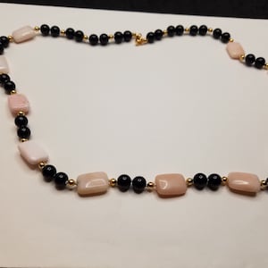 May include: A necklace made of black and pink rectangular beads with gold accents.