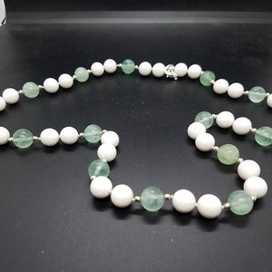 May include: A white and green beaded necklace with a silver clasp. The necklace is made of round beads, with alternating white and green beads.