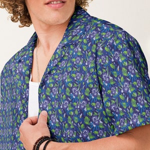Könnte beinhalten: Ein kurzärmeliges Hemd mit blauem und grünem Blumendruck und einem Kragen. Das Hemd hat eine lockere Passform und ist aus einem leichten Stoff gefertigt.