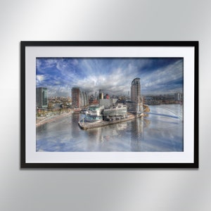 May include: A panoramic view of a modern city skyline with a bridge and a large building in the foreground. The sky is blue with white clouds. The water is calm and reflects the buildings and sky.
