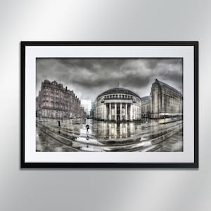 Könnte beinhalten: Gerahmtes Schwarz-Weiß-Foto einer Stadtstraßenszene an einem regnerischen Tag. Das Bild zeigt mehrere große Gebäude, darunter ein kuppelförmiges Bauwerk mit Säulen. Menschen mit Regenschirmen gehen auf dem nassen Pflaster.