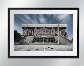 May include: A black and white photograph of a brick building with a large sign that reads "Aston Villa". The building is surrounded by a parking lot and a cloudy sky.