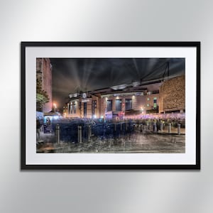 May include: A night time view of a large stadium with a crowd of people gathered outside. The stadium is lit up with spotlights and the crowd is blurred in motion.
