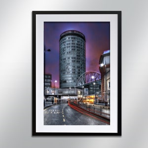 Può includere: Una fotografia di un edificio moderno e alto con le parole "Bullring Bullring" sul lato. L'edificio è illuminato di notte e ci sono auto che passano per la strada sottostante. L'edificio si trova nella città di Birmingham, in Inghilterra.