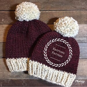Pode incluir: Dois chapéus de tricô com pompons. Os chapéus são bordô com uma faixa branca e pompons brancos. Os chapéus estão sobre uma superfície de madeira. O texto "Knitting Pattern" está em um círculo branco com uma coroa ao redor.