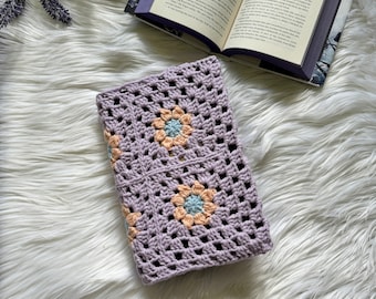 May include: A lavender crocheted book cover with a granny square pattern and pastel peach and blue flowers.