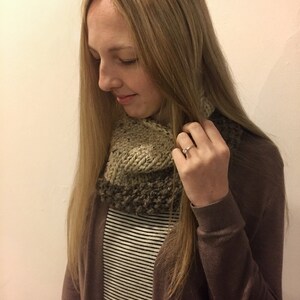 May include: A woman wearing a brown cardigan over a striped shirt and a knitted cowl neck scarf in shades of brown and beige.