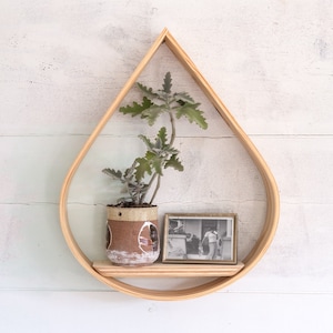 May include: A wooden teardrop-shaped shelf with a small potted plant and a black and white photo on it. The shelf is mounted on a white wall.