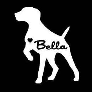 May include: A white silhouette of a dog with the name "Bella" in cursive script and a small heart. The dog is in a standing pose with one paw raised, set against a black background.