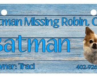 May include: Blue wooden dog tag with the text "Batman Missing Robin, CGC" and "Batman" in a larger font. The tag also includes a photo of a small, brown and white chihuahua, the owner's name "Traci", and a phone number "402-926-9920".
