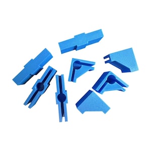 May include: A collection of bright blue plastic corner clamps and connectors, designed for joining materials at right angles. The set includes various shapes, such as L-shaped and rectangular pieces, all in a solid, vibrant blue color. These are likely used for woodworking or crafting projects.