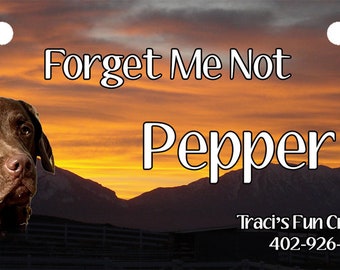 May include: Rectangular license plate with a brown dog portrait and the name "Pepper." The background features a sunset over mountains. Text reads "Forget Me Not" and "Traci's Fun Creations."