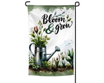 May include: A garden flag with a watercolor design of a watering can pouring water on flowers. The text "Bloom & Grow" is written in black script on the flag.