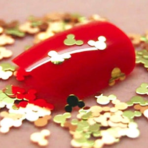 May include: Red nail polish with gold Mickey Mouse shaped glitter on top. The glitter is also scattered around the nail.