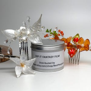 May include: A collection of handmade hair accessories, including a silver flower comb, a star-shaped hair clip, and an orange and red flower comb. A silver tin with the text "DIP IT FANTASY FILM" is also present.