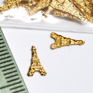 May include: Two gold-coloured Eiffel Tower charms. The charms are small and detailed, with a textured surface.