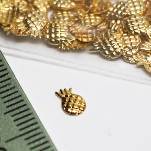 May include: A close-up of a small, gold-coloured pineapple charm. The charm is about 1.25 cm in size and has a detailed design.