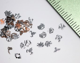 May include: A collection of silver metal zodiac signs, including a crab, a lion, a scorpion, a scale, and a fish. The signs are scattered on a white surface.